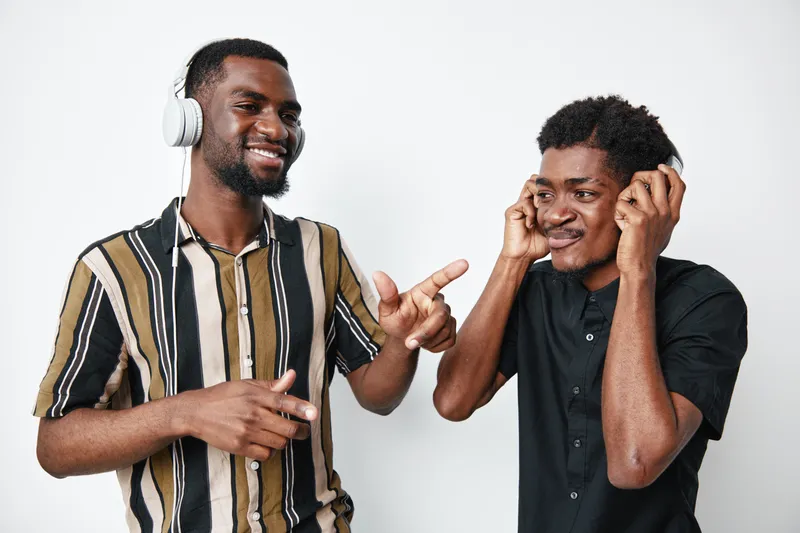 Two young black men with dark skin enjoying music together wearing headphones and smiling in casual clothes on white background in studio.