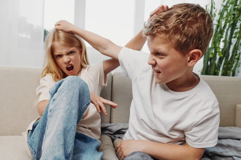 Angry boy and girl fighting on couch at home, faces showing frustration and aggression, concept of sibling conflict and childhood emotions.