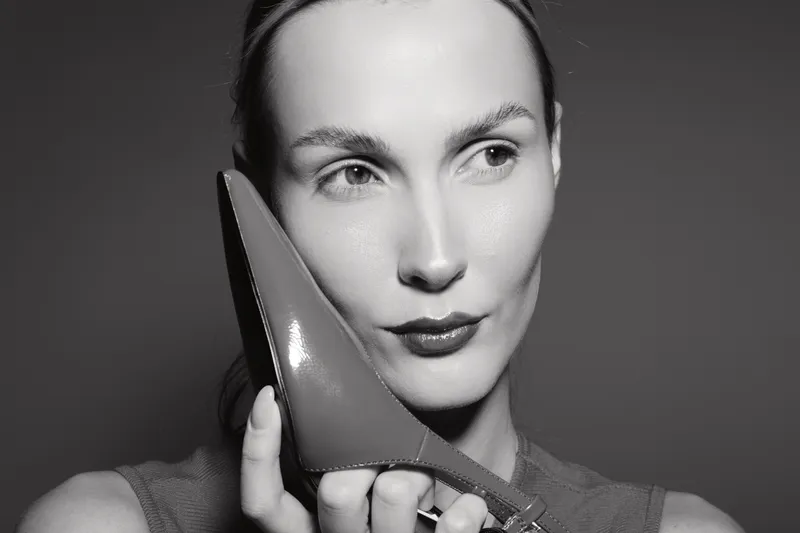 Closeup of a fair skinned caucasian woman holding a pointed shoe near her face in black and white.