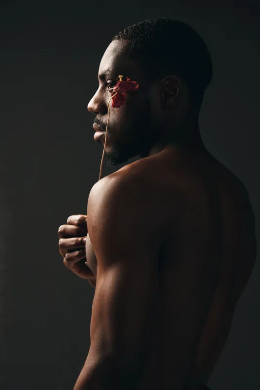 Creative conceptual portrait of African man with dark skin and artistic red paint on face, showing visual style and emotion in studio lighting with bare shoulders and side profile.