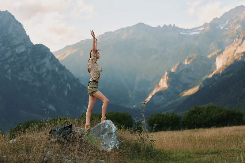 Woman in casual clothes standing on a rock with arms raised in a mountain valley. Concept of lifestyle, freedom, and outdoor adventure in nature.