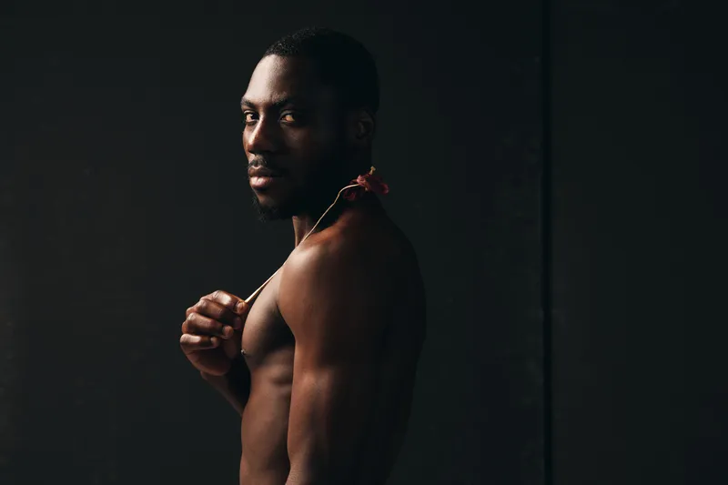 African man with dark skin and muscular body posing shirtless in creative conceptual visual style. Portrait with dramatic lighting and serious expression on black background for artistic photography.