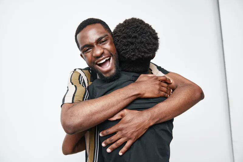 Two black men hugging each other with happy expressions and dark skin tones on white background for friendship and connection concept.
