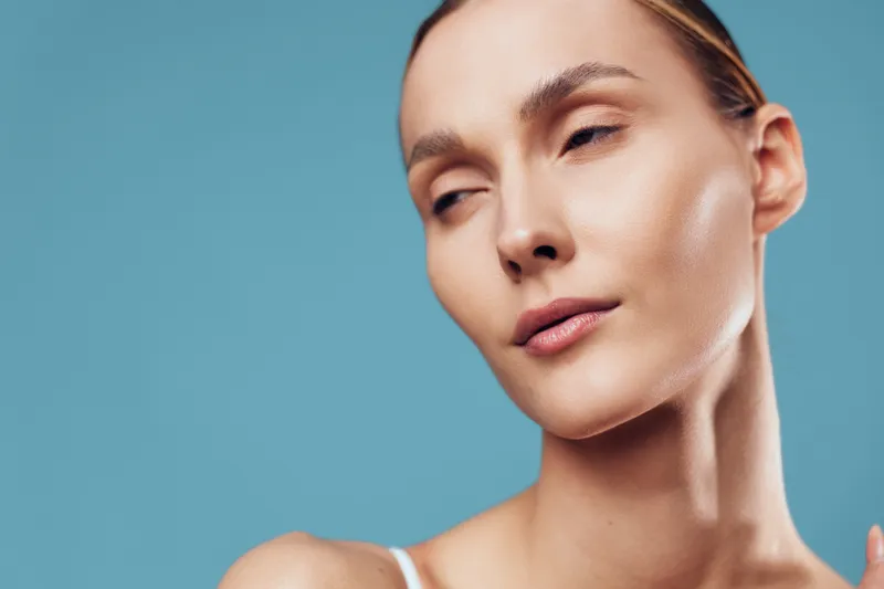 Closeup of calm woman with flawless skin and closed eyes posing against blue background, showing natural beauty and serene expression in studio lighting.