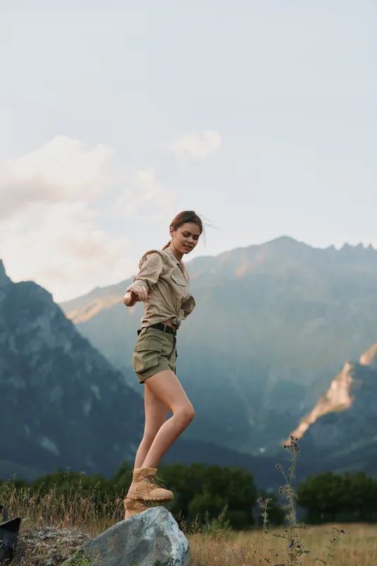 Vibrant woman enjoying the outdoors in a mountain landscape, smiling with relaxed posture, sunlit breeze, casual outfit, natural colors, scenic terrain, carefree mood