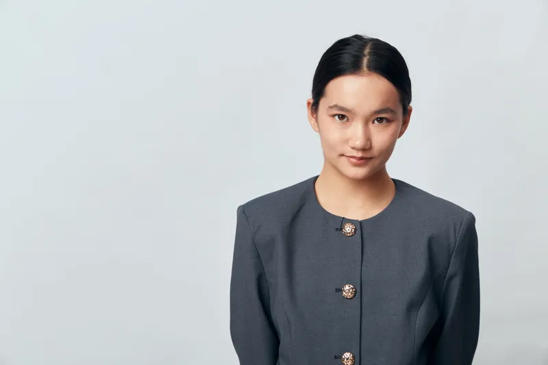 Young woman portrait with neat hairstyle and gray jacket looking confident on plain light background for business, professional, beauty and fashion concept.