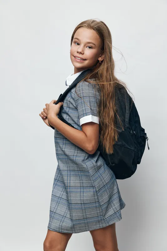 Girl, child, backpack and smile standing in studio for school, education and casual outfit. Portrait of happy kid with long hair wearing dress and carrying bag for learning.