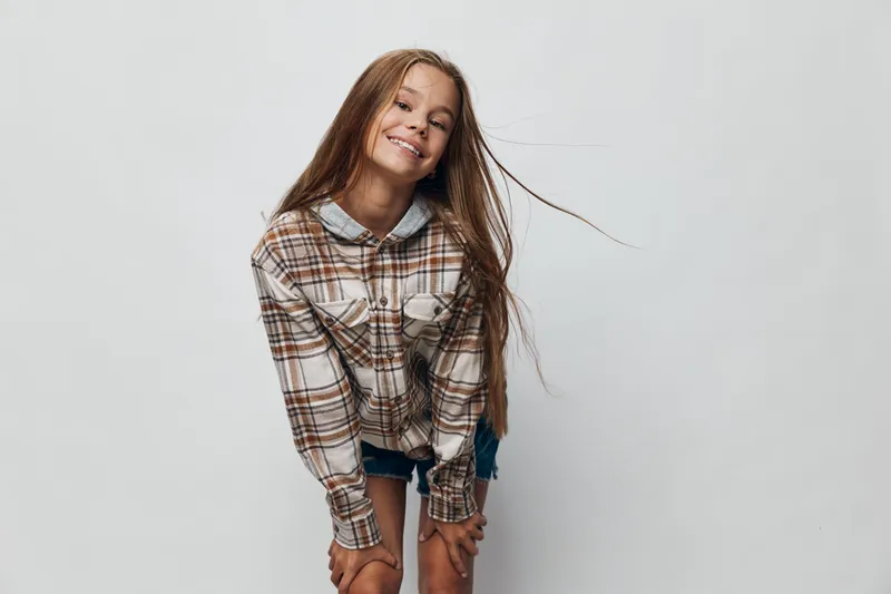 Girl with long hair wearing plaid shirt and denim shorts smiling happily on white background showing joyful teenager fashion and youth style casual portrait.