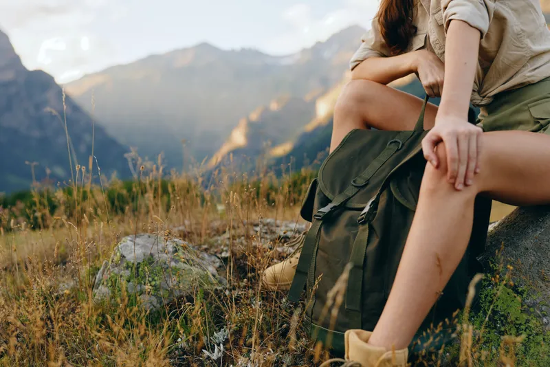 Woman lifestyle sitting outdoors on rock, relaxed posture, casual clothing, mountain landscape background, warm natural light, peaceful moment