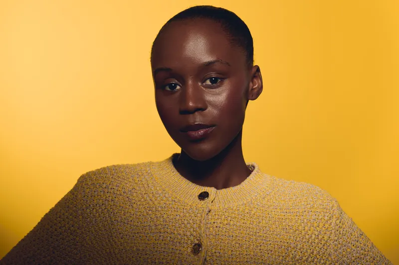 Portrait of confident dark skinned African woman wearing textured yellow sweater against yellow background. Studio lighting highlights natural skin texture and calm expression. Concept of beauty.