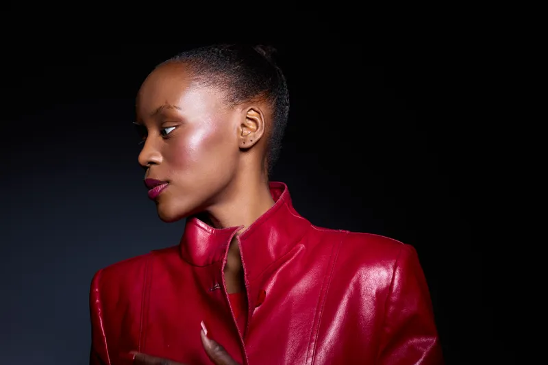 Portrait of a confident black woman with dark skin wearing a red leather jacket, looking to the side against a dark background. Concept of fashion, elegance, and beauty.