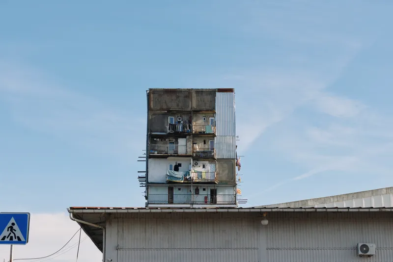 Industrial architecture, stack of containers on a warehouse rooftop, weathered metal, urban silhouette against a clear sky, gritty texture and architectural contrast