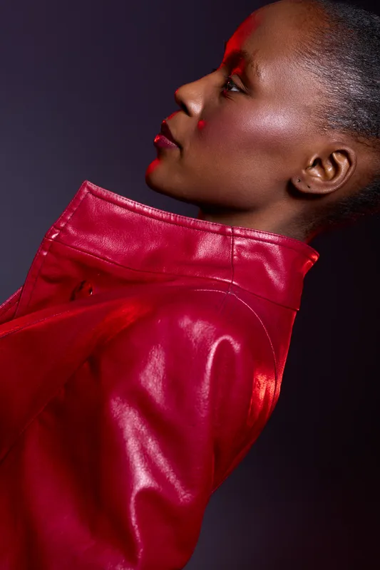 Profile of a dark skinned African woman wearing a red leather jacket. Studio portrait with dramatic lighting on black background. Concept for fashion, style, and confidence.