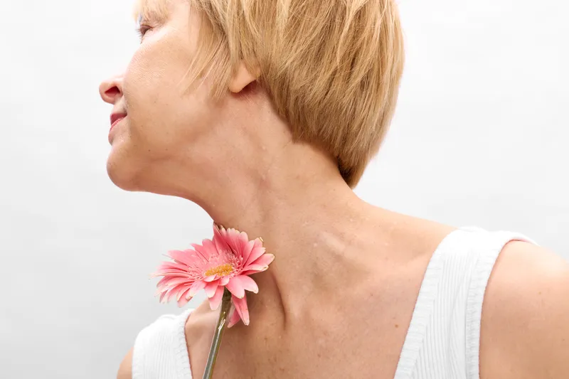 Woman flower profile spring closeup blond neck tenderness fresh beauty, side profile portrait holding pink gerbera on collarbone, isolated on white background