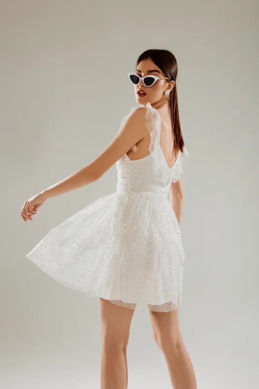 Young woman in a white lace dress and sunglasses poses turning back. Studio shot on a neutral background. Concept for woman beauty fashion and summer style.
