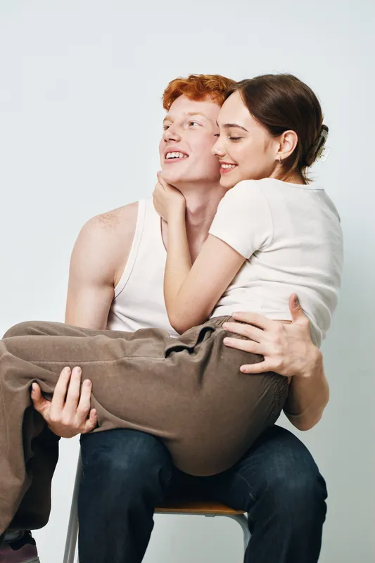 Couple, young man carrying woman sitting on chair, smiling and embracing each other with casual clothes on white background.