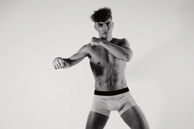 Young man with muscular body posing in underwear, fitness model showing strength and confidence in studio with monochrome background and dramatic lighting.
