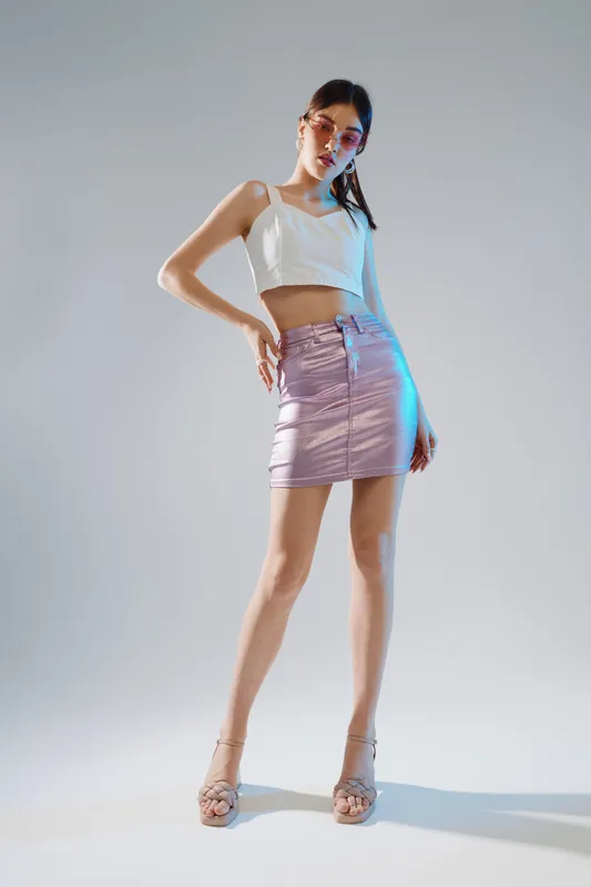 Young woman in a white crop top and metallic skirt poses confidently on a light background. Fashion concept featuring beauty, style, and modern trends in clothing and accessories.
