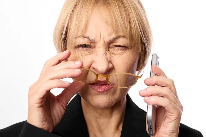 Senior woman smartphone communication worried hand mouth, bright studio lighting, aging lifestyle, stressed expression, health concern, close up portrait, soft background