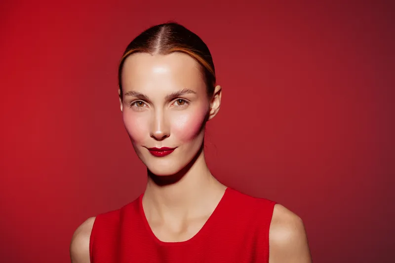 Portrait of a confident woman with slicked back hair wearing a red sleeveless top against a red background. Concept of fashion, beauty, elegance, and minimalism in studio lighting.