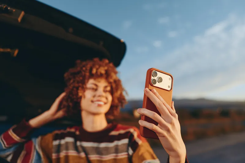 Woman lifestyle outdoor selfie, smiling curly hair woman holds smartphone in hand, portrait near street bus stop, golden evening light, casual striped shirt, relaxed travel mood