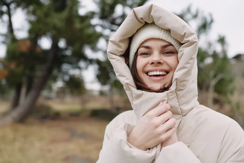 Happy person in a warm beige hooded jacket outdoors, smiling in a chilly setting, cozy winter fashion and outdoor lifestyle shot with natural light and casual expression