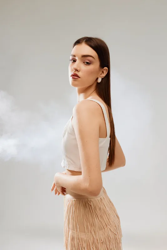 Young woman beauty fashion model with long straight hair poses in beige outfit on light background. Studio portrait with soft natural makeup and elegant earrings. Concept of style.