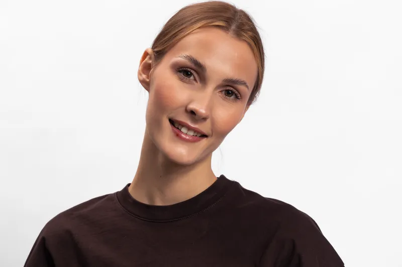 Smiling young woman with blonde hair wearing dark sweater looks at camera on white background. Studio portrait with natural makeup and friendly expression for lifestyle and beauty concept.