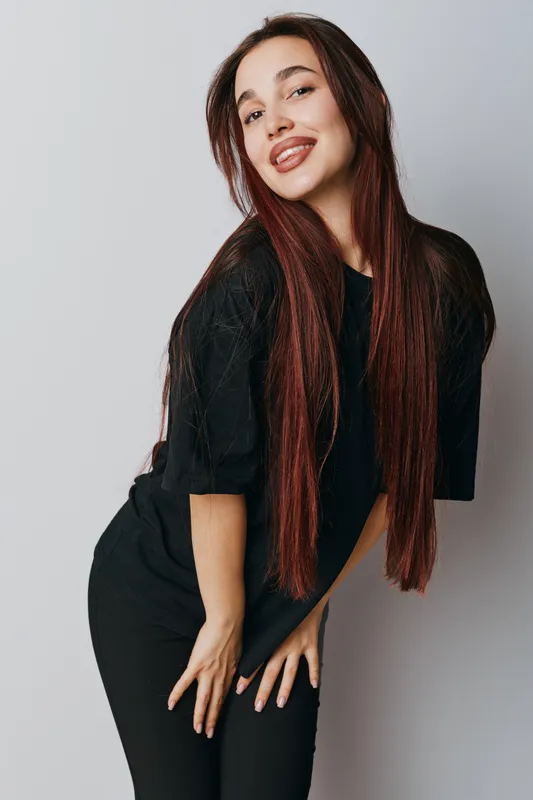 Young woman with long straight hair wearing black outfit posing and smiling on light background. Beauty, fashion and casual style with confident expression and natural look in studio.