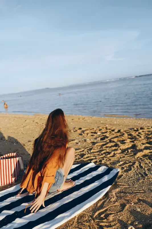 Woman, beach, ocean, sunlight, summer, relaxation, towel, horizon, standing, back, female adult with long hair reclining on striped towel, warm sand, gentle waves, calm mood