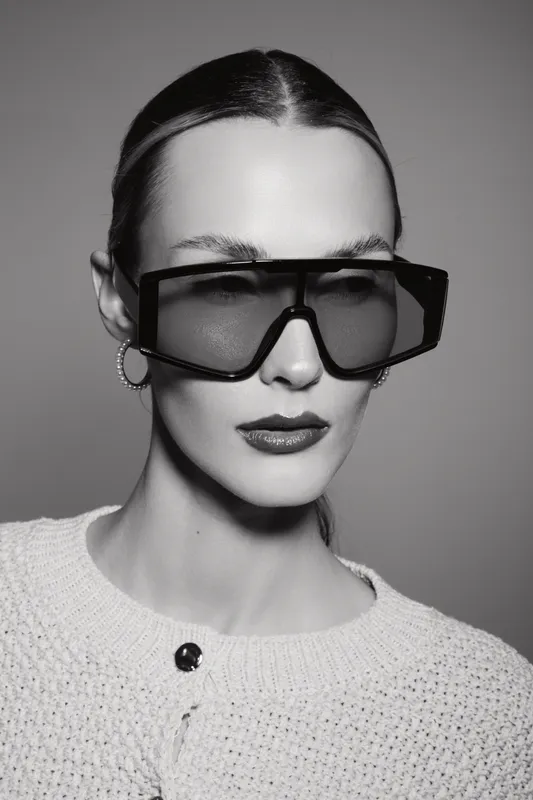 Portrait of a fair skinned Caucasian woman wearing oversized geometric sunglasses and a knitted top. Studio lighting creates a fashion and style concept with a modern minimalistic mood.