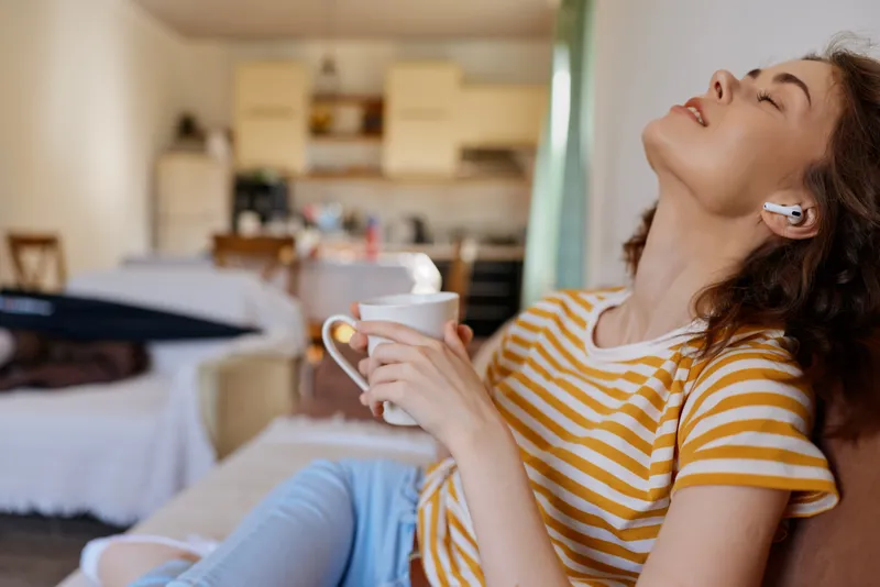 Bright, relaxed moment with a woman indoors at home, enjoying a warm coffee mug, casual striped tee, and soft light. A cozy lifestyle scene focused on comfort and calm.