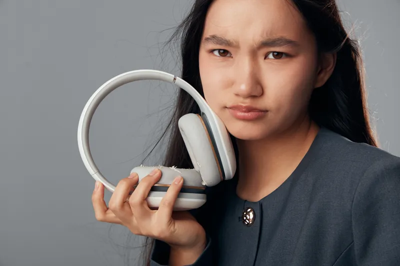 Young woman holding headphones in hand with serious facial expression against gray background, listening device and technology accessory closeup for audio and music enjoyment.