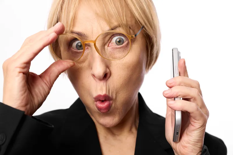 Woman with glasses, surprised blonde, eyewear on face, holding office technology smartphone, closeup, white background, business suit, shock expression, studio light