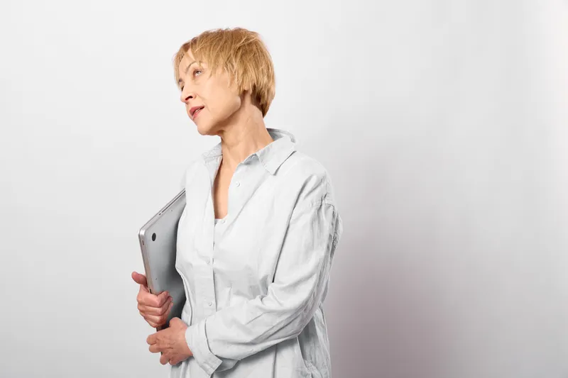 Smiling woman with short blond hair holding a tablet in a studio portrait, side pose, white background, relaxed office style, modern technology mood, soft light, quietly today