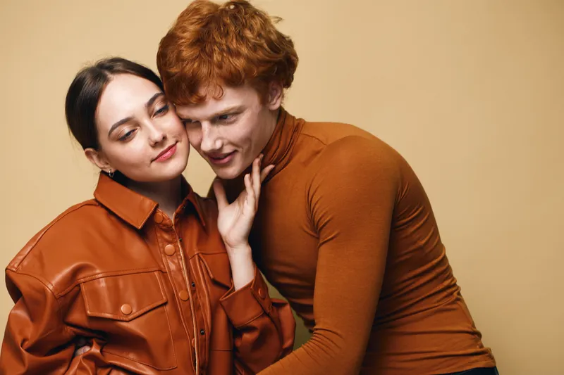 Couple, woman and man cuddling close with warm clothing and cozy feeling in studio. Fashion, love, connection, affectionate moment, intimacy with stylish outfits on beige background.