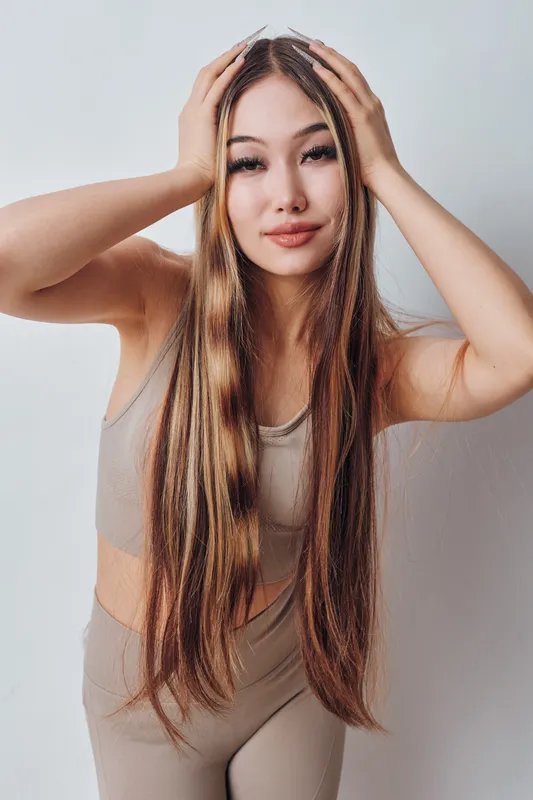 Young woman with long braided hair posing in beige sportswear on white background. Portrait of confident female model with natural makeup and trendy hairstyle for fashion and beauty.