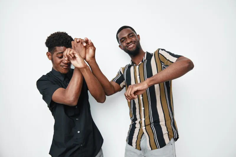 Two young black men dancing and having fun together in casual clothes on white background. African ethnicity, dark skin, friendship and joyful mood in studio.