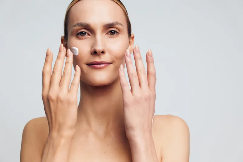Woman skincare beauty portrait close up, she applies cotton pads to face with hands, clean healthy skin, soft natural makeup, studio light, calm expression on white background