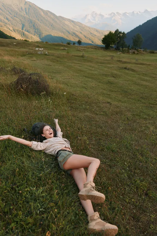 Woman in a relaxed outdoors lifestyle scene in a meadow, joyful smile under sunlight, nature and mountains backdrop, casual wear, open space