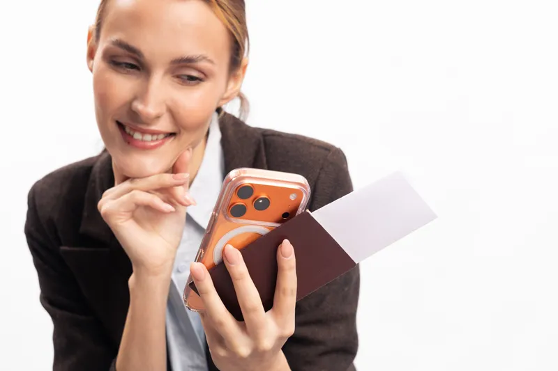 Smiling woman holding passport and smartphone looks thoughtfully while preparing for travel. Concept of planning, vacation, and holiday with travel documents on white background.