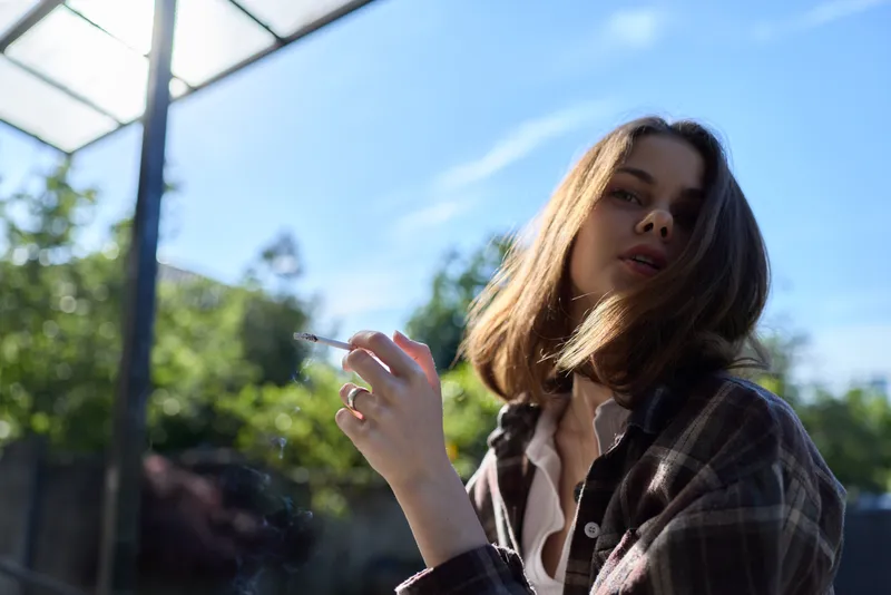 Casual woman outdoors in a plaid shirt. Close-up portrait under bright daytime sunlight, conveying relaxed lifestyle, natural style, and fresh mood. Soft light highlights hair and skin, suggesting