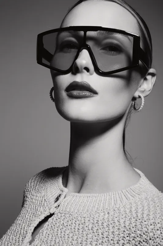 Portrait of a fair skinned caucasian woman wearing oversized sunglasses and knitted sweater against plain background.