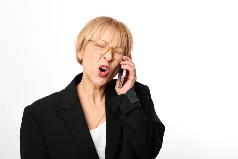 Elderly woman in business suit and glasses, speaking on a phone, isolated on white background, indoors, mature professional, confident call, clean portrait