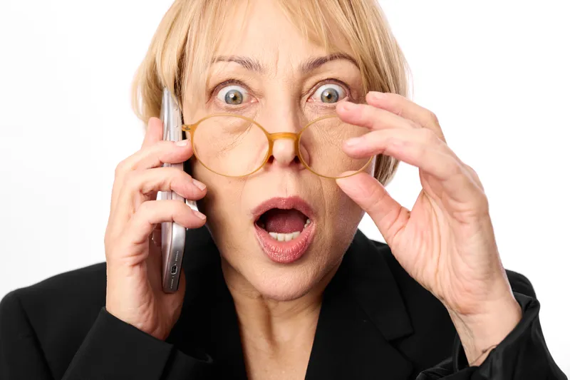 Woman businesswoman surprised elderly, holding glasses frames with both hands, talking phone call, communication multitasking, close up portrait on white background, office suit style