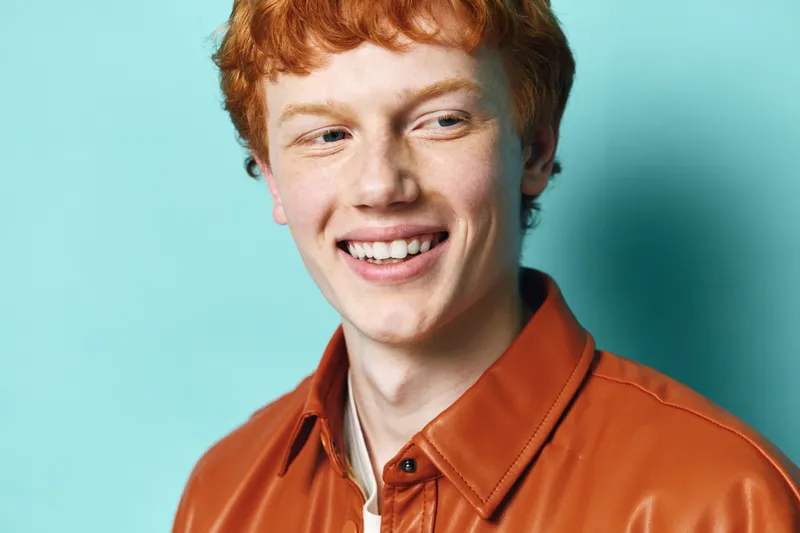 Young man with red hair and freckles smiling looking away on blue background. Portrait of cheerful male with casual orange shirt and friendly expression for lifestyle and happiness.