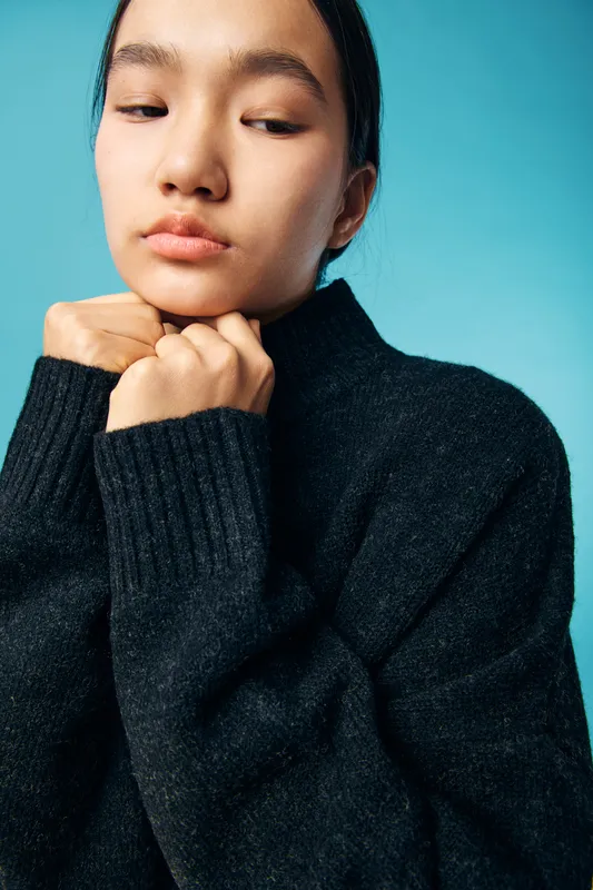 Portrait of young woman with calm expression wearing black sweater on blue background. Closeup, fashion, beauty, minimalism and casual style with soft lighting and natural look studio setup.