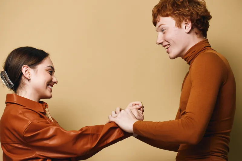 Young man and woman smiling and holding hands, interaction and connection with joy and friendship on plain light background in casual clothing for relationship.