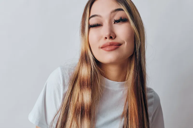 Young woman with long hair wearing white t shirt posing with closed eyes and subtle smile on light background. Beauty, youth and casual fashion for lifestyle portrait.