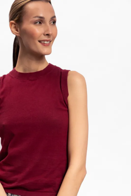 Smiling young woman in sleeveless red top looks aside with soft expression. Studio portrait on white background. Concept for fashion, casual style, and positive emotions in lifestyle.